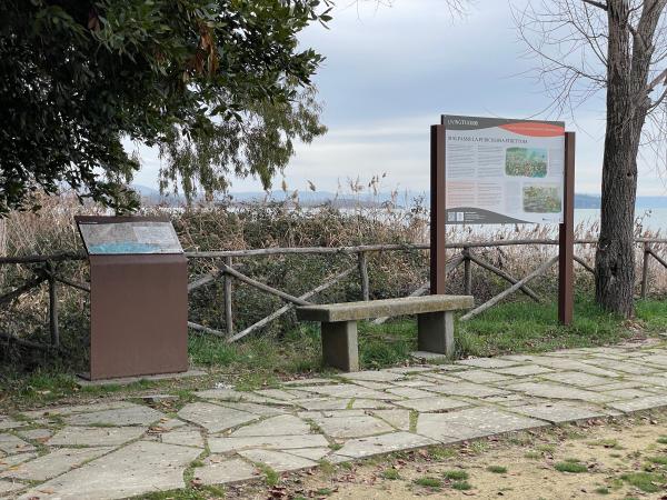 Rest area at Malpasso with bench, information boards and fence separating from reedbed and lake.